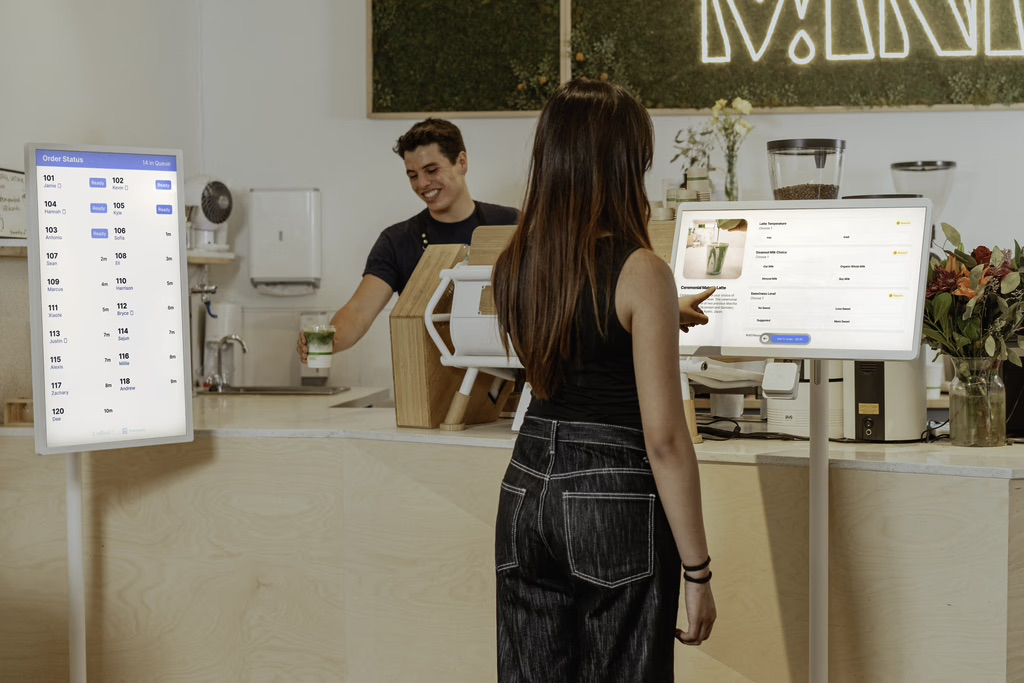 A guest ordering at a Snackpass kiosk while staff prepare drinks behind the counter